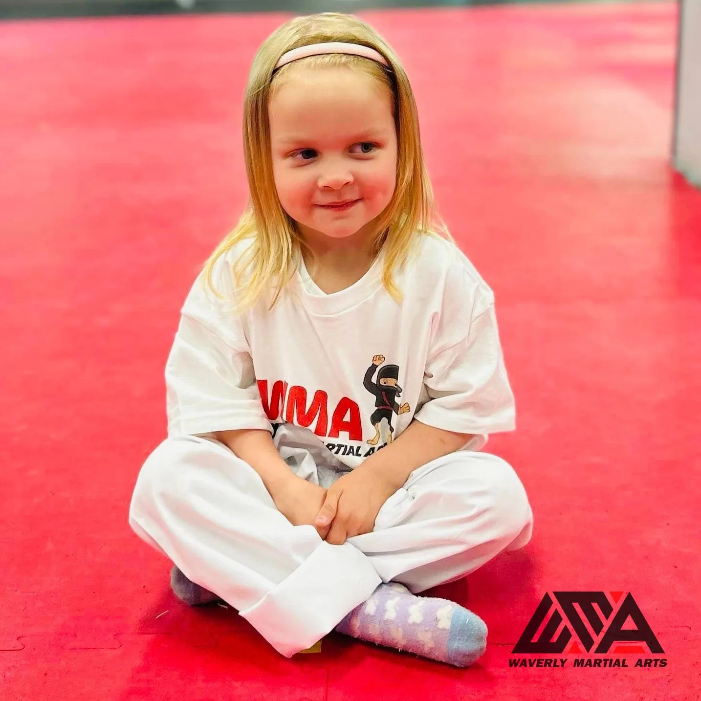 A smiling young student sitting on the red mat at Waverly Martial Arts in Patchogue
